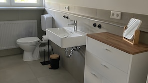 A modern bathroom with a toilet, sink, and storage cabinet. - Modern Apartment with Balcony Near Nuremberg – Ideal for Families, Business & Trade Fair Guests (Heroldsberg)