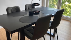 A modern dining area with a black table, matching chairs, and a black side table with a basket. - Modern Apartment with Balcony Near Nuremberg – Ideal for Families, Business & Trade Fair Guests (Heroldsberg)