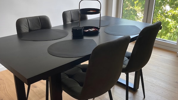 A modern dining area with a black table, matching chairs, and a black side table with a basket.