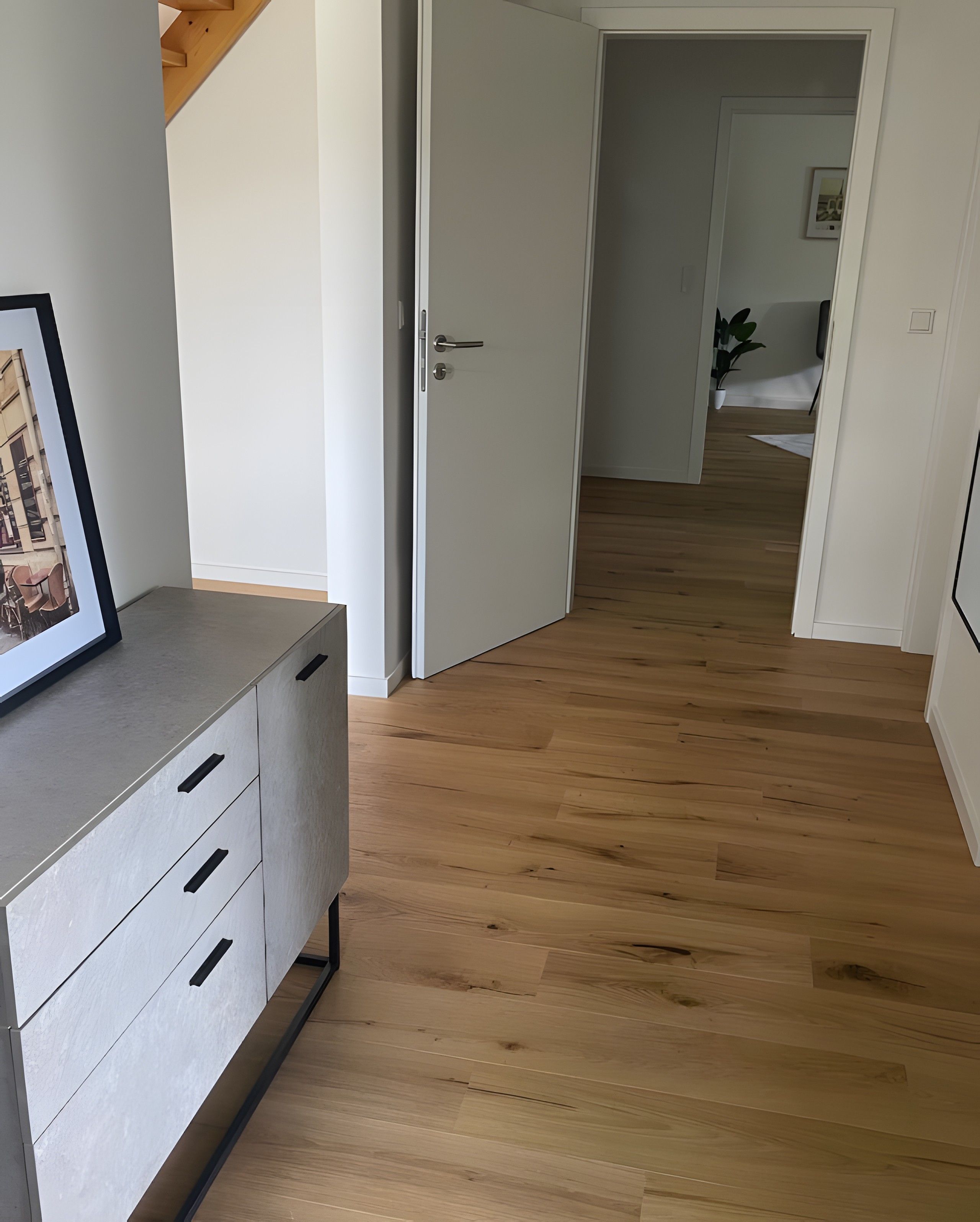 Ein Flur mit Holzboden, einer weißen Tür und einem grauen Schrank mit Schubladen.