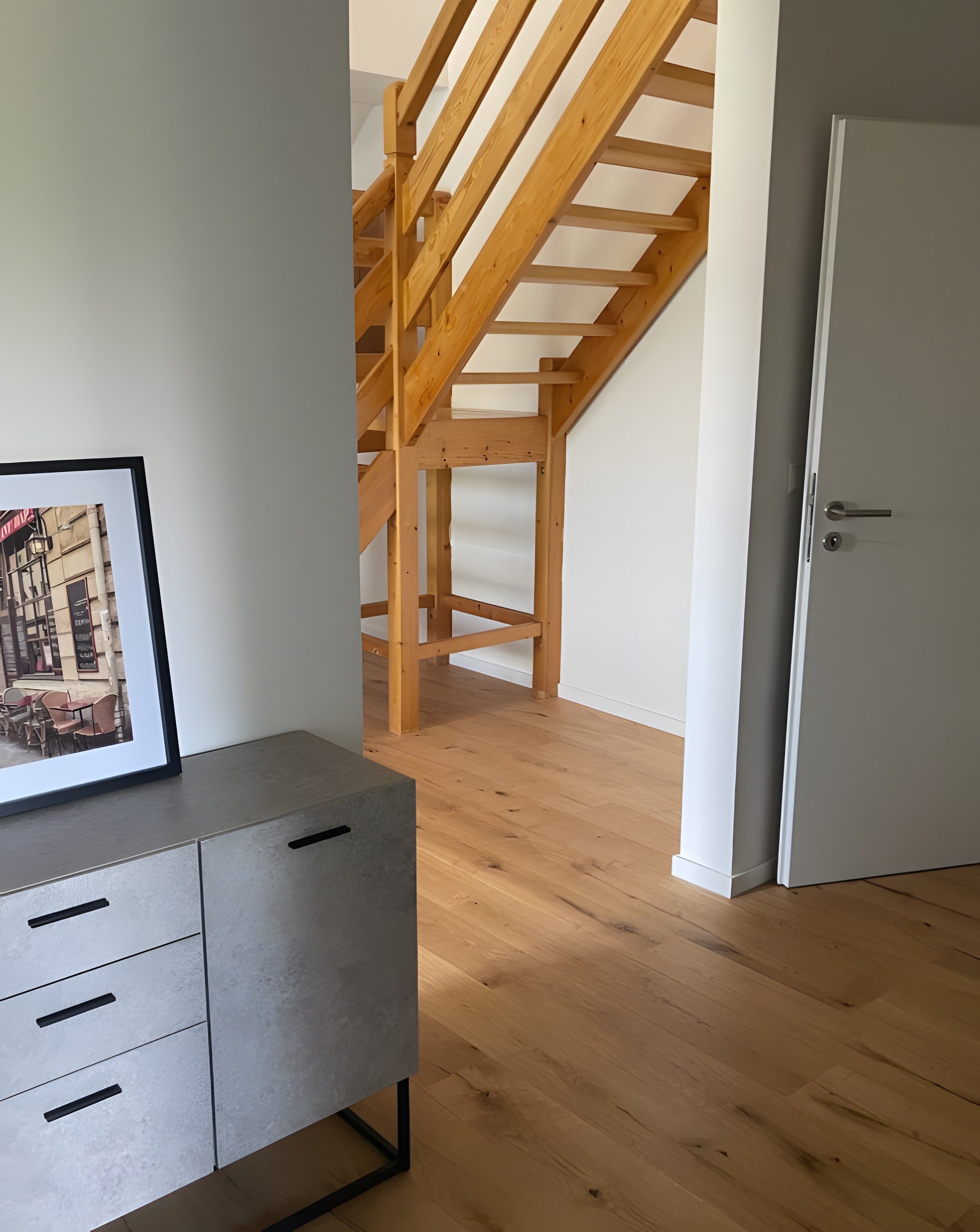 Um quarto com uma escada de madeira, um armário cinza com gavetas e uma porta branca.