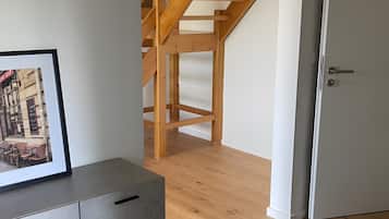 Um quarto com uma escada de madeira, um armário cinza com gavetas e uma porta branca.