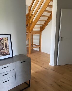 A room with a wooden staircase, a grey cabinet with drawers, and a white door.