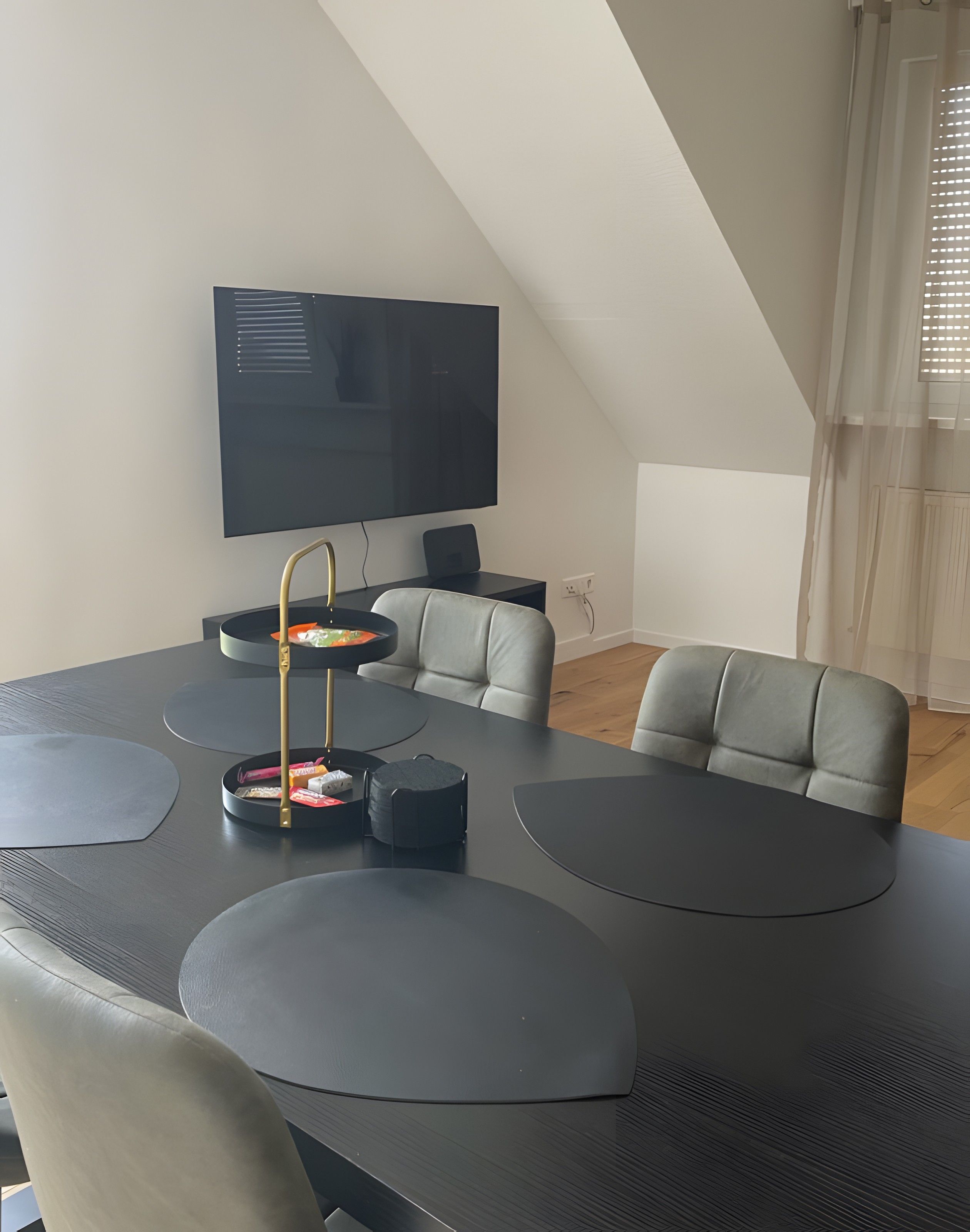 Ein modernes Wohnzimmer mit einem großen schwarzen Tisch, grauen Sofas und einem flachbildfernseher an der Wand.