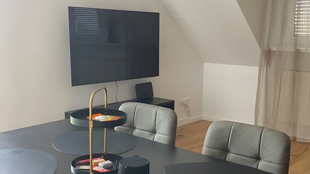 Ein modernes Wohnzimmer mit einem großen schwarzen Tisch, grauen Sofas und einem flachbildfernseher an der Wand.