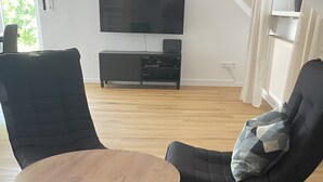 Ein modernes Wohnzimmer mit einem runden Holztisch, zwei schwarzen Sesseln und einem schwarzen Sofa.