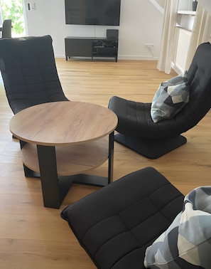 A modern living room with a round wooden table, two black armchairs, and a black sofa. - Modern Apartment with Balcony Near Nuremberg – Ideal for Families, Business & Trade Fair Guests (Heroldsberg)