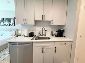A compact kitchen with white cabinets, a stainless steel dishwasher, a coffee maker, and a toaster. - Luxury Studio | 1 Bed | Northern Liberties (Philadelphia)
