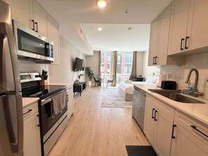 A modern kitchen with stainless steel appliances, a flat-screen TV, and a dining area with a view of the city. - Luxury Studio | 1 Bed | Northern Liberties (Philadelphia)