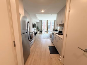 A modern kitchen with a refrigerator, stove, and microwave. There is a dining area with a table and chairs, and a window with curtains. - Luxury Studio | 1 Bed | Northern Liberties (Philadelphia)