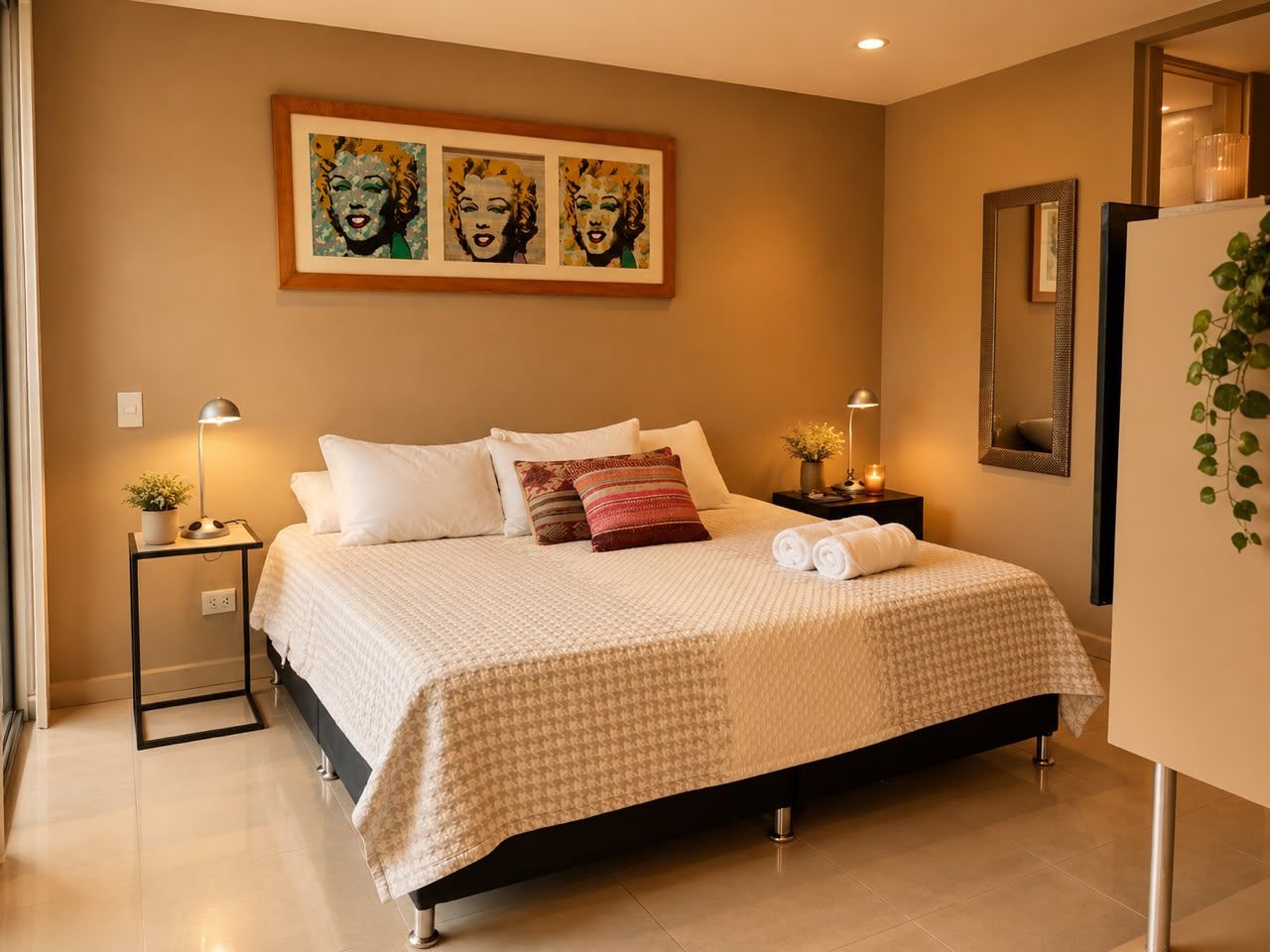 Quarto com cama, mesas de cabeceira, espelho e obras de arte na parede.