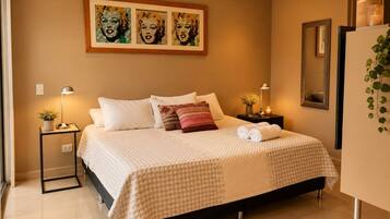 Quarto com cama, mesas de cabeceira, espelho e obras de arte na parede.