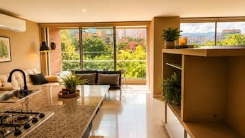 A modern kitchen with a large island, a dining area with a sofa, and a view of a cityscape through large windows.