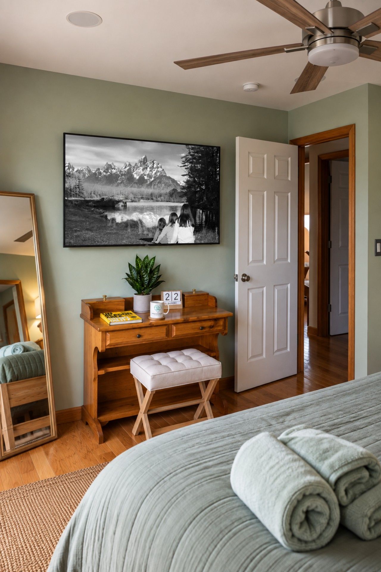 Een slaapkamer met een bed, een bureau met een plant, een lijst met foto aan de muur en een deur die naar een andere kamer leidt.