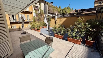 Un'area patio con tavolo e sedie, circondata da piante in vaso e vista sugli edifici.