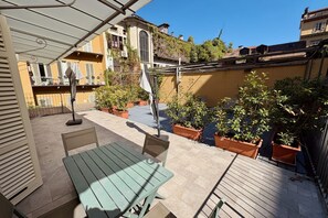 Un'area patio con tavolo e sedie, circondata da piante in vaso e vista sugli edifici.