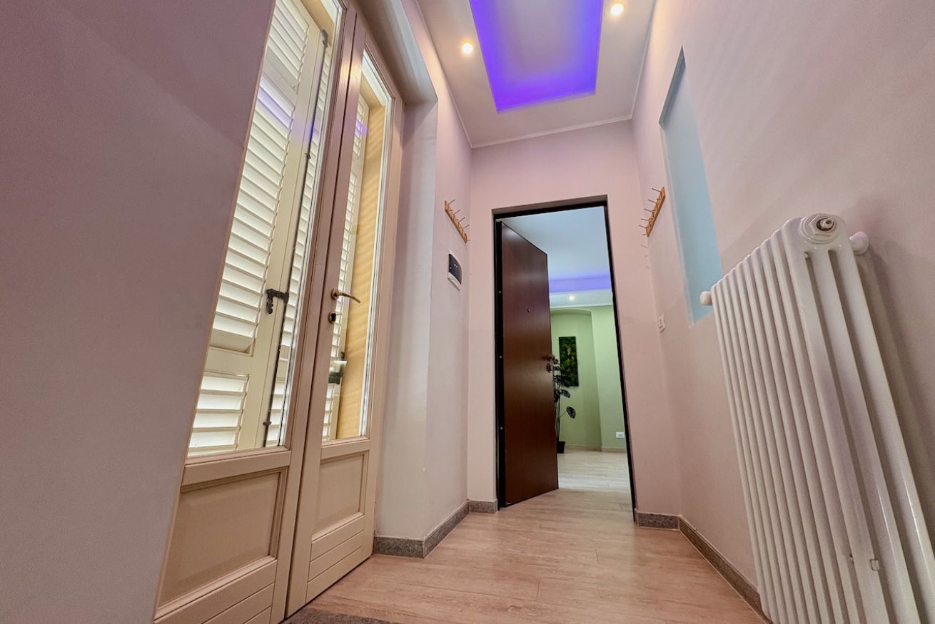 Un corridoio con una porta che dà su una stanza, un termosifone sulla parete e un lampadario al soffitto.