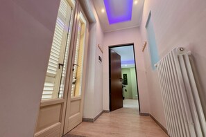 Un corridoio con una porta che dà su una stanza, un termosifone sulla parete e un lampadario al soffitto.
