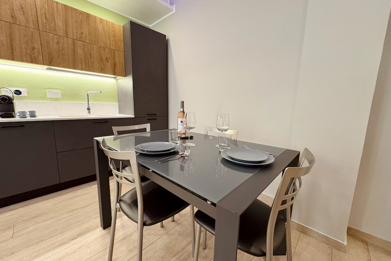 Zona pranzo moderna con tavolo scuro, quattro sedie e una bottiglia di vino.