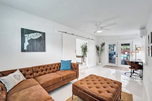 Een moderne woonkamer met een bruine leren bank, een bijpassend poef en een plafondventilator.