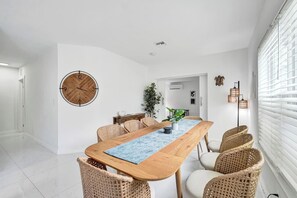 Un espace repas moderne avec une table en bois, des chaises en osier et une grande horloge murale.