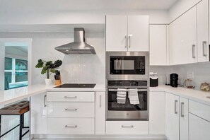A modern kitchen with stainless steel appliances, white cabinetry, and a window with blinds. - Coastal Bay Retreat | Pool | 8 Min to Beach (Fort Lauderdale)