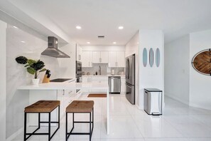 A modern kitchen with white cabinets, stainless steel appliances, and a central island with stools. - Coastal Bay Retreat | Pool | 8 Min to Beach (Fort Lauderdale)