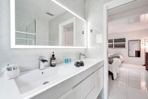 Une salle de bain moderne avec un grand miroir, un plan de toilette en marbre blanc et un espace douche.