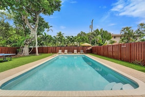 A rectangular swimming pool with a wooden deck surrounding it, a wooden fence, and a grassy area with trees. - Coastal Bay Retreat | Pool | 8 Min to Beach (Fort Lauderdale)