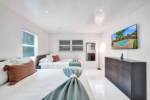 Een moderne slaapkamer met twee bedden, een televisie en een groot raam met jaloezieën.