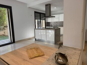 A modern kitchen with a central island, a stainless steel range hood, and a view of the outdoors through large windows. - Malaga, duplex (Tunis)