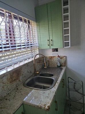 Una cocina con un lavamanos, una ventana con persianas y armarios verdes.