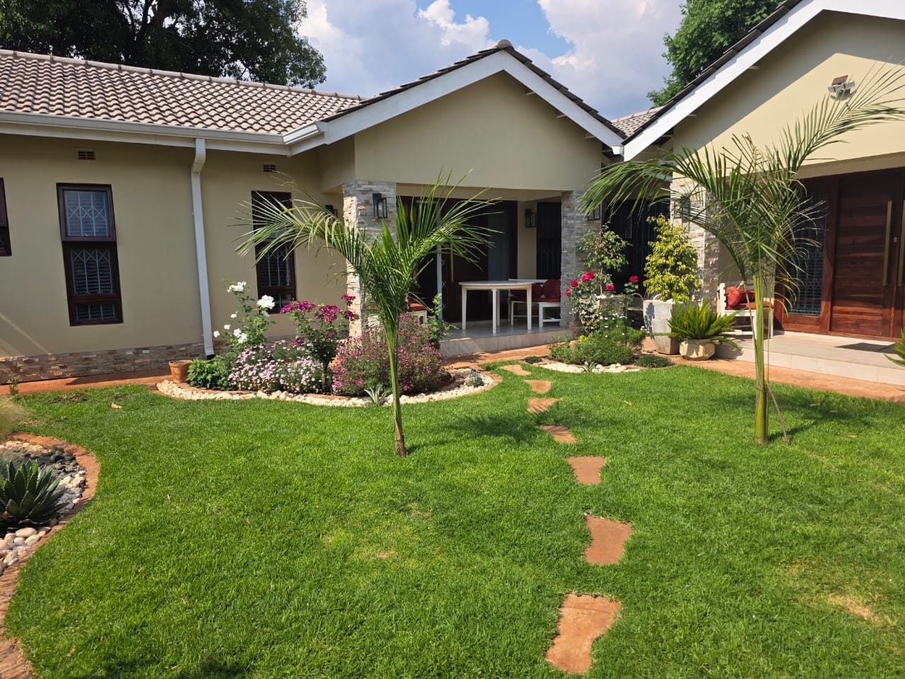A residential property with a well-maintained lawn, a patio area with a table and chairs, and a variety of plants and flowers.