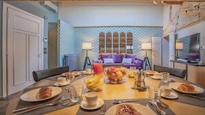 Un comedor con una mesa redonda dispuesta para el desayuno, un sofá con cojines y una pared estampada al fondo.