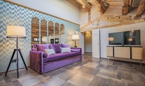 Ein modernes Interieur mit einem violetten Sofa, einer Stehlampe, einem Fernseher und einer Holzbalkendecke.