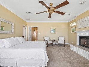 A bedroom with a large bed, two chairs, a fireplace, and a ceiling fan. - Lafitte Beach Retreat (Pensacola Beach)