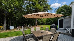 Een terras buiten met een tafel, stoelen, een parasol en een barbecue.
