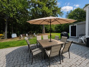 An outdoor patio with a table and chairs, a covered umbrella, and a barbecue grill. - Family Friendly getaway right across from community beach, pet-friendly with trail access (Beaver Cove)