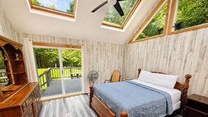 Een slaapkamer met een houten bed, een dressoir en een ventilator. Er zijn dakramen en uitzicht op de omgeving.