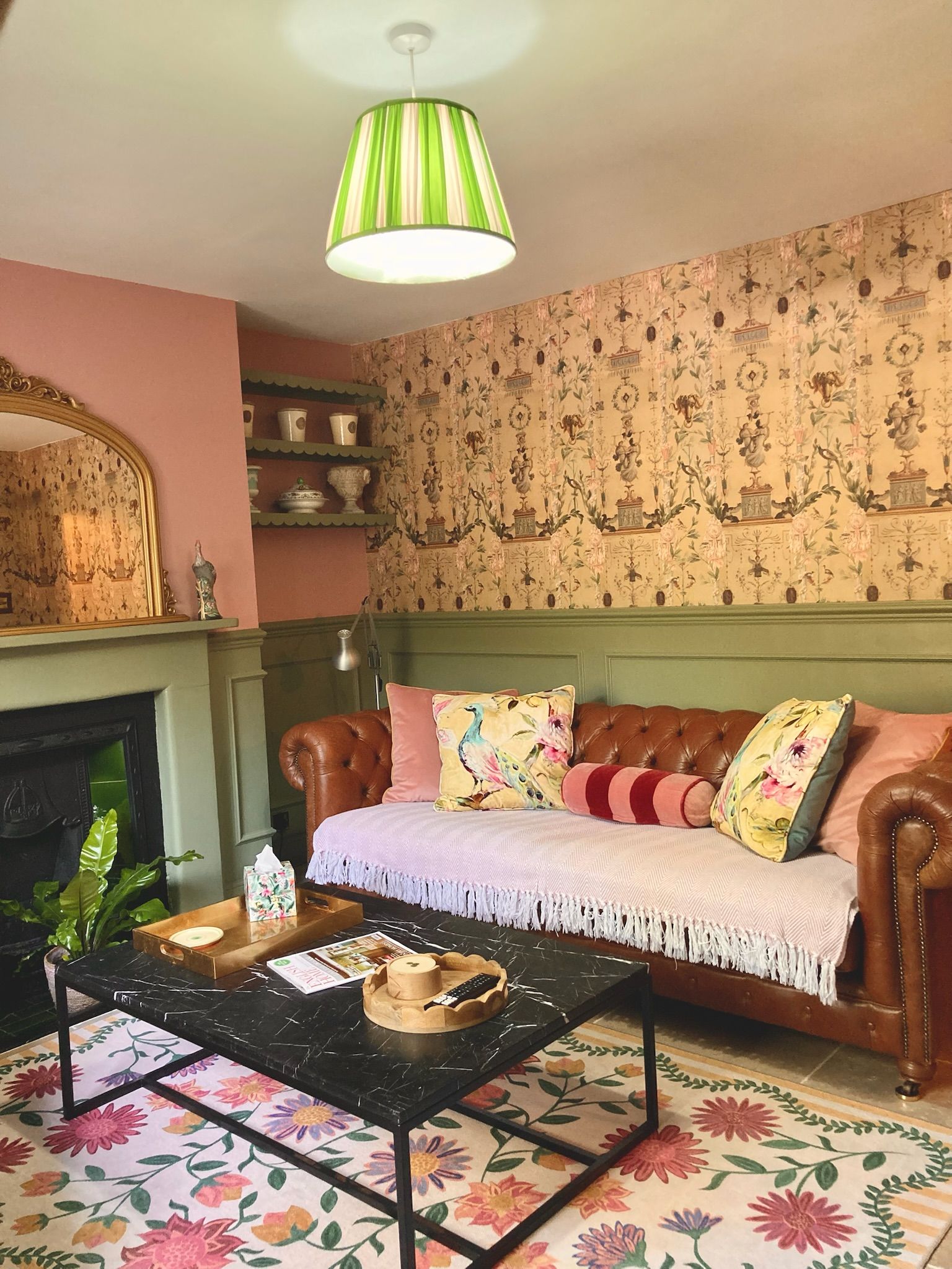 A cozy living room with a sofa, a coffee table, a fireplace, and floral wallpaper.