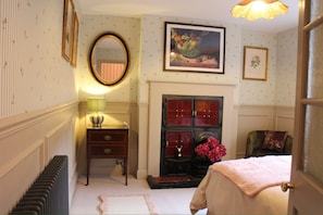 A bedroom with a fireplace, a mirror, a dresser, and a bed. - Beautiful Cosy Pittville Garden Flat | Walking Distance To Town & Racecourse (Cheltenham)