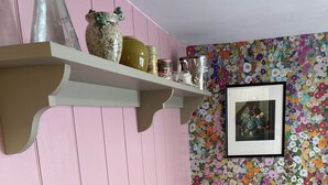 Ein Zimmer mit einer rosafarbenen Wand, einem Holzstuhl, einem runden Tisch mit Marmorplatte und einer blumengemusterten Wand.