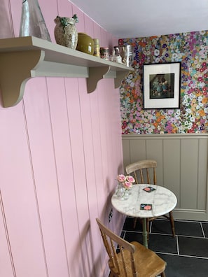 A room with a pink wall, a wooden chair, a round table with a marble top, and a floral-patterned wall. - Beautiful Cosy Pittville Garden Flat | Walking Distance To Town & Racecourse (Cheltenham)