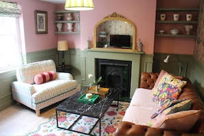 A cozy living room with a fireplace, a sofa, a chair, and a coffee table. - Beautiful Cosy Pittville Garden Flat | Walking Distance To Town & Racecourse (Cheltenham)