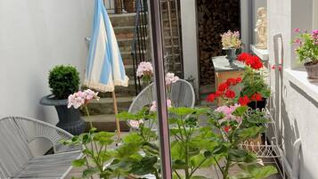 A view through a window of a balcony with potted plants, a chair, and a statue.