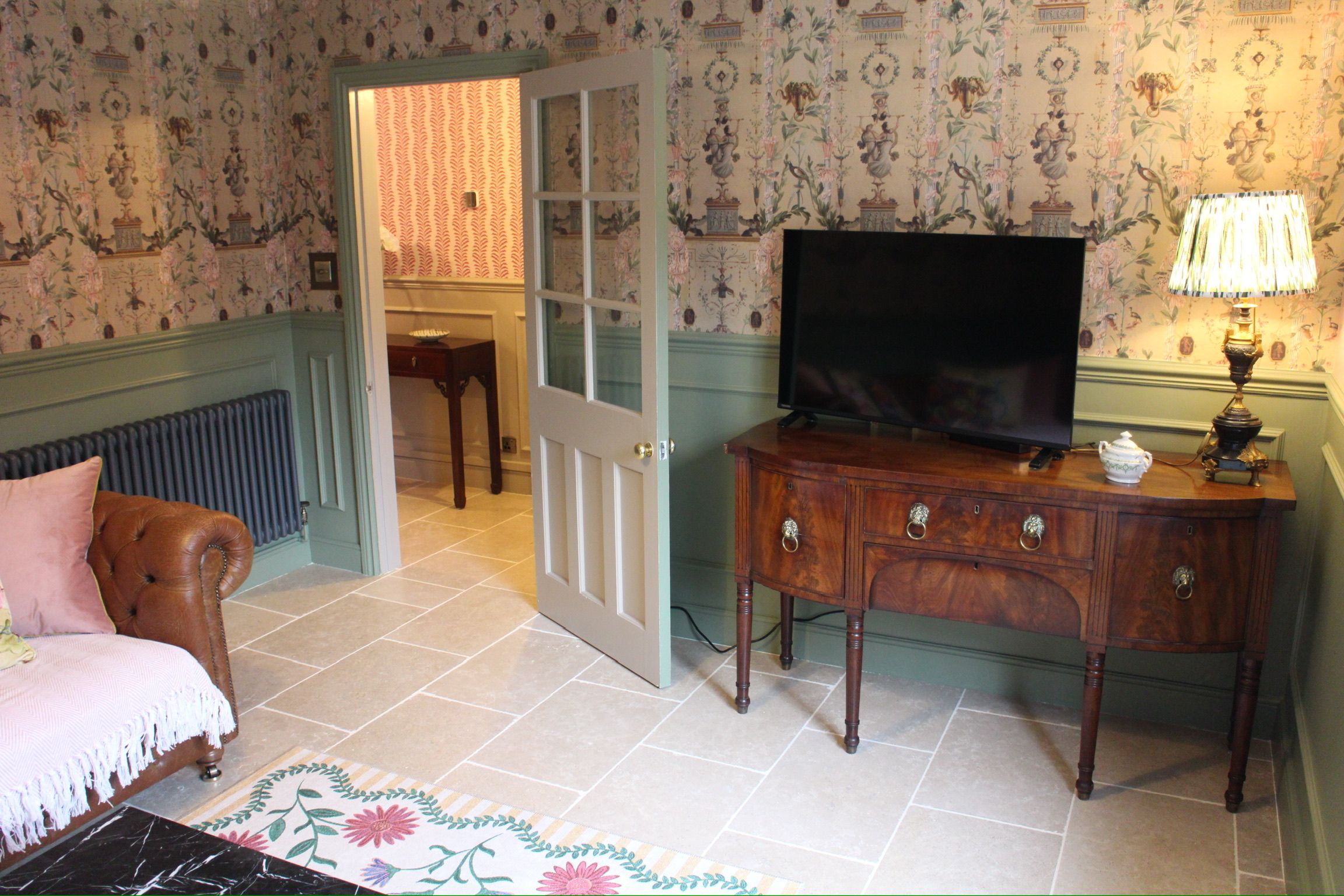Een kamer met een televisie op een houten kast, een deur naar een andere kamer en een radiator.