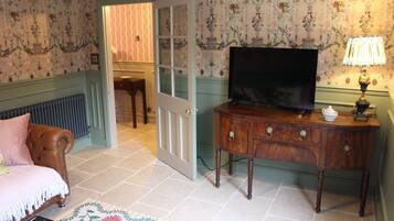 Een kamer met een televisie op een houten kast, een deur naar een andere kamer en een radiator.