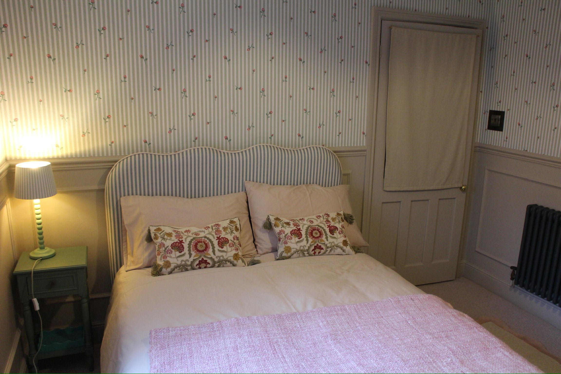 Une chambre à coucher avec un lit, deux oreillers, une lampe de chevet et un radiateur.