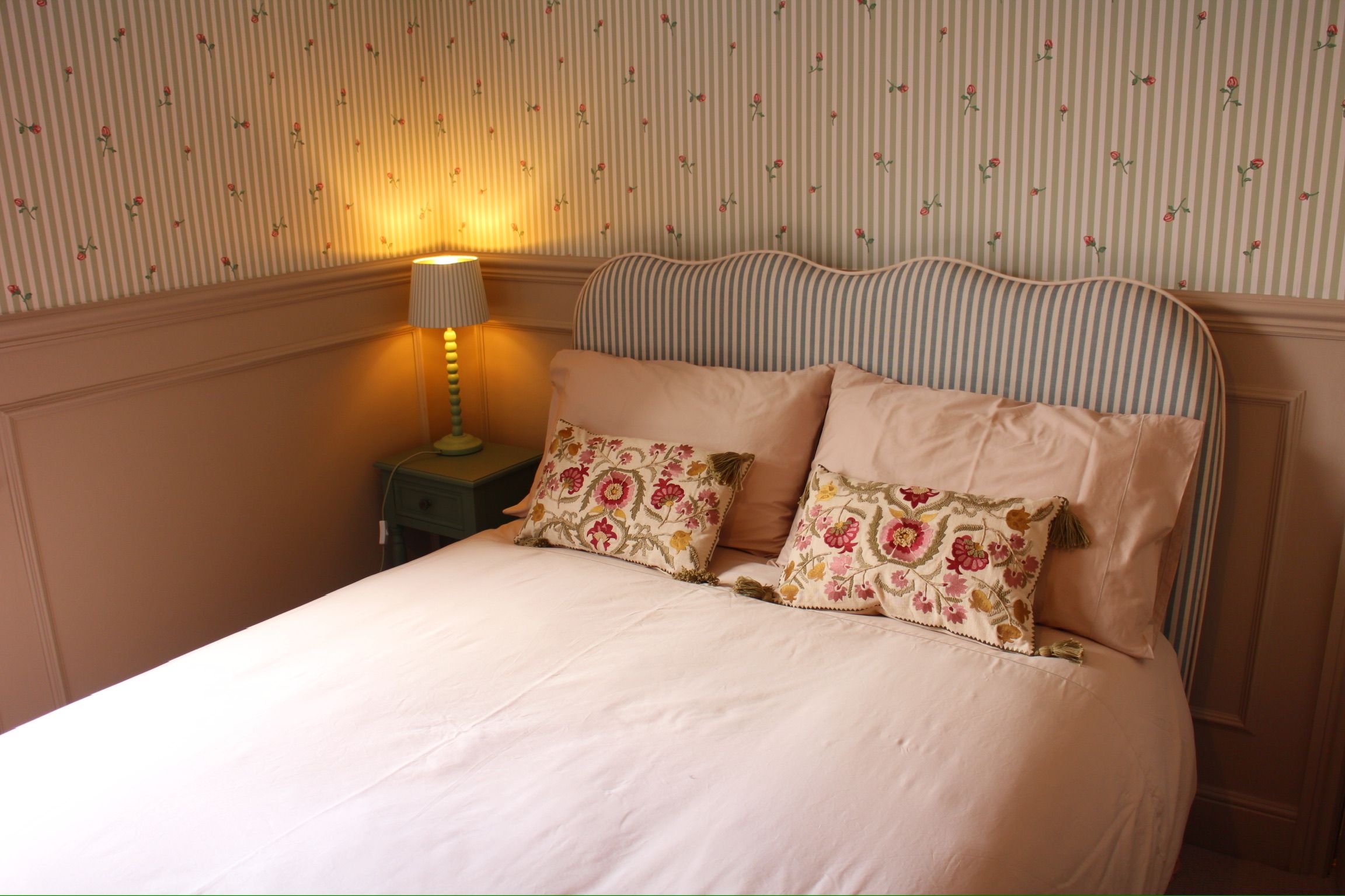 A bed with floral-patterned pillows, a striped headboard, and a bedside lamp on a nightstand.