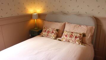 A bed with floral-patterned pillows, a striped headboard, and a bedside lamp on a nightstand.